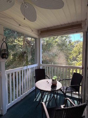 A covered outdoor seating area with a table and chairs, surrounded by a white railing, overlooking a forested area. - Coastal 2B condo minutes from the beach & attractions with pool and golf access! (Longs)