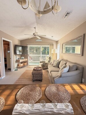 A spacious living room with a ceiling fan, a television, a sofa, and a dining area with woven placemats. - Coastal 2B condo minutes from the beach & attractions with pool and golf access! (Longs)