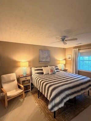 A bedroom with a bed, two bedside tables, a chair, a ceiling fan, and a window with curtains. - Coastal 2B condo minutes from the beach & attractions with pool and golf access! (Longs)