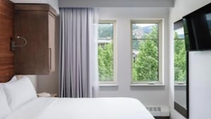 Ein Hotelzimmer mit einem Bett, einem Holzschrank, zwei Fenstern und Blick auf Grünfläche.