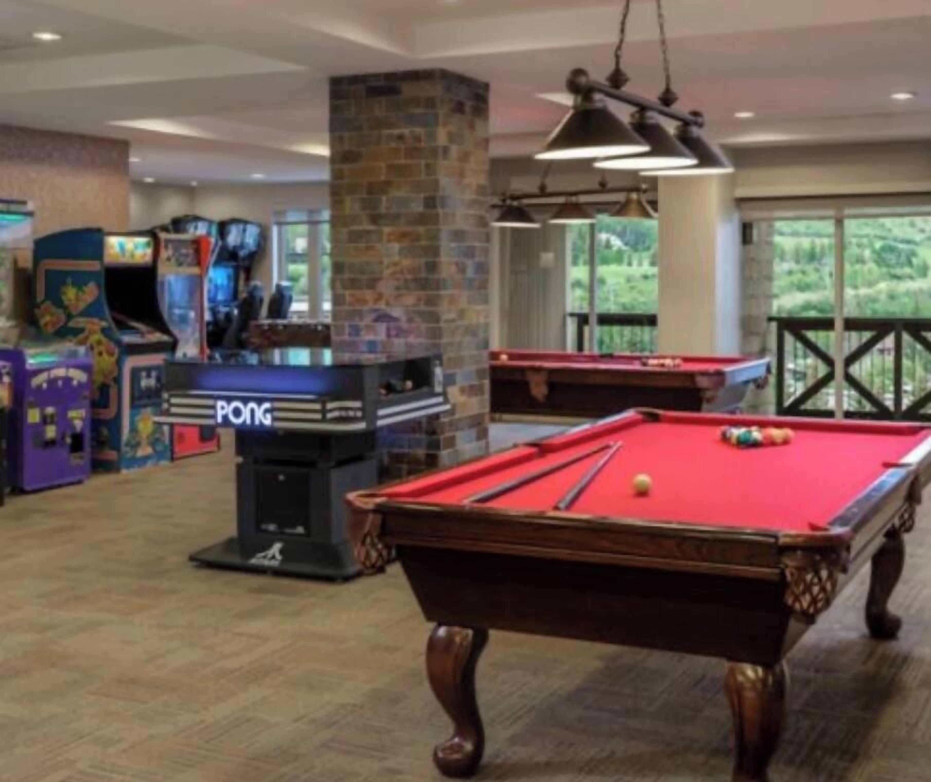 Een pooltafel met een rode viltbekleding, een pingpongtafel en achtergrondspektakel van spelautomaten.