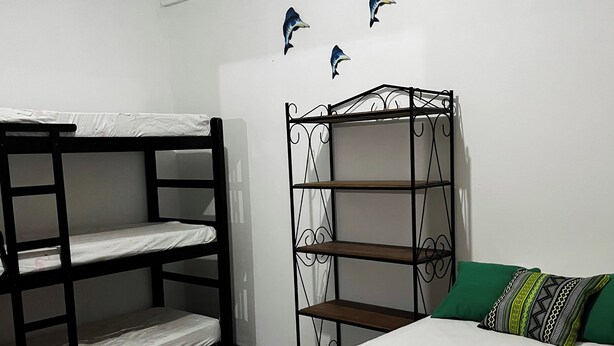 Quarto com beliches, estante de metal, tapete estampado e cama com travesseiro verde.
