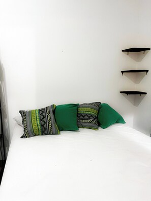 A bed with a white mattress, three pillows with geometric patterns, and three black wall-mounted shelves. - Studio apartment in Paraty Mirim, 10 minutes from the beach. (Paraty-Mirim)