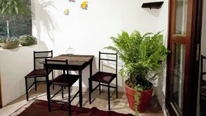 Uma pequena área de refeições com mesa e cadeiras de madeira, uma planta em vaso e uma parede com detalhes decorativos.