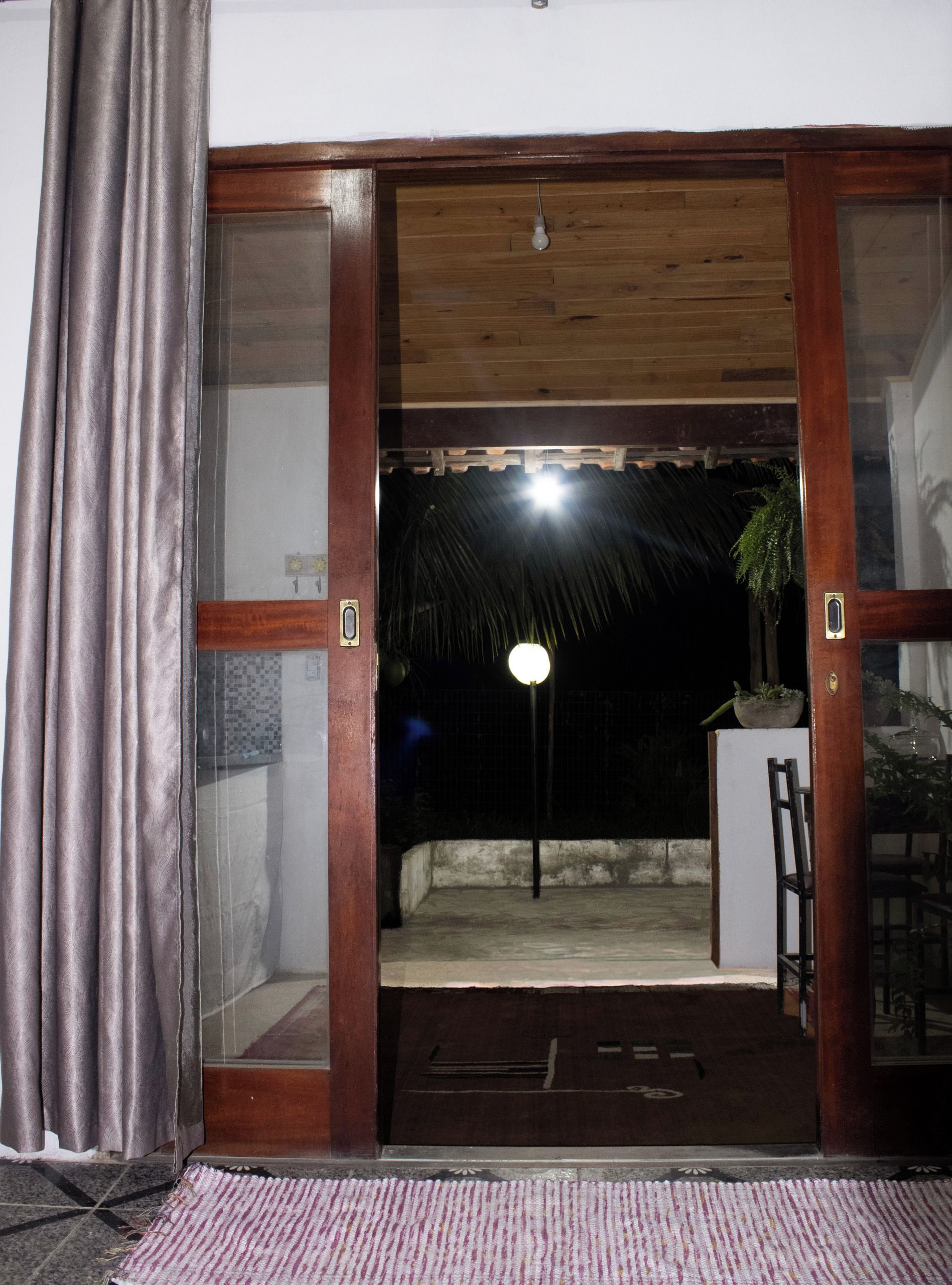 Una porta que dona a un espai exterior amb un teulat de palla, una planta en test i una cadira.