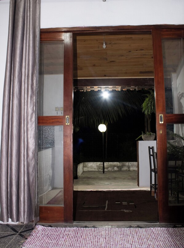 A doorway leading to an outdoor area with a thatched roof, a potted plant, and a chair.
