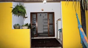 A yellow-walled hallway with a wooden door, a potted plant, and a hammock. - Studio apartment in Paraty Mirim, 10 minutes from the beach. (Paraty-Mirim)