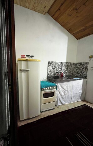A compact kitchen with a refrigerator, stove, and a tiled backsplash. - Studio apartment in Paraty Mirim, 10 minutes from the beach. (Paraty-Mirim)