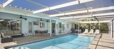 Una piscina interior con un patio cubierto, una mesa de comedor y sillones de descanso.