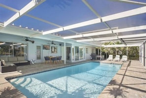An indoor swimming pool with a covered patio area, a dining table, and lounge chairs. - Waterfront Cape Coral Oasis: Heated Pool, Spa, Direct Gulf Access & Dock (Cape Coral)