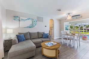 A modern living room with a grey sectional sofa, a wooden coffee table, and a dining area with white chairs. - Waterfront Cape Coral Oasis: Heated Pool, Spa, Direct Gulf Access & Dock (Cape Coral)