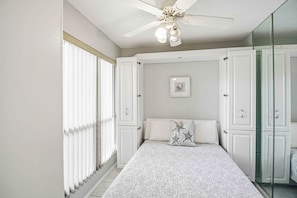 A bedroom with a bed, a ceiling fan, a window with blinds, and a mirror.