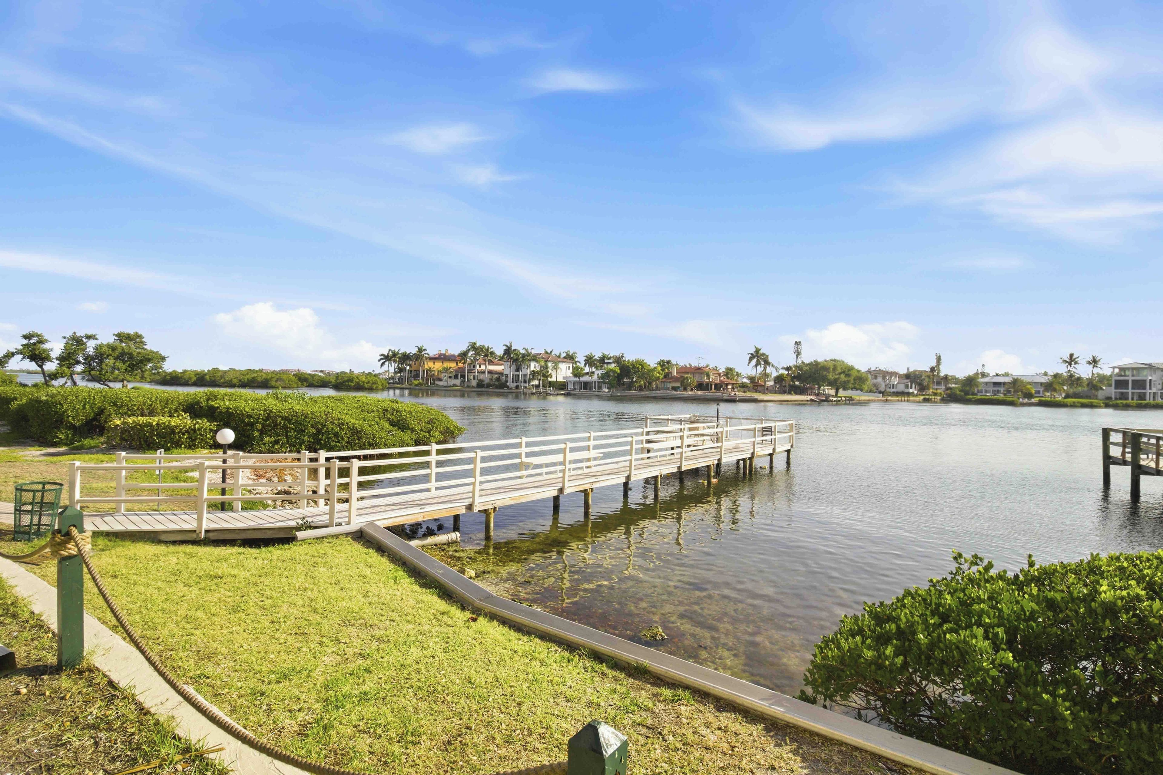 A waterfront park with a wooden dock, grassy areas, and a calm lake.