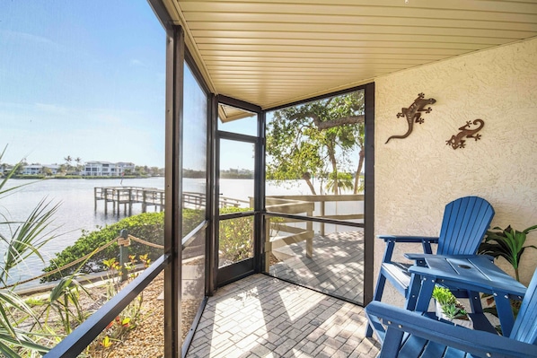 A covered outdoor area with a view of a lake, a dock, and a chair.