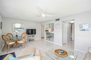 A living room with a television, dining area with chairs, a sofa, and a glass coffee table.