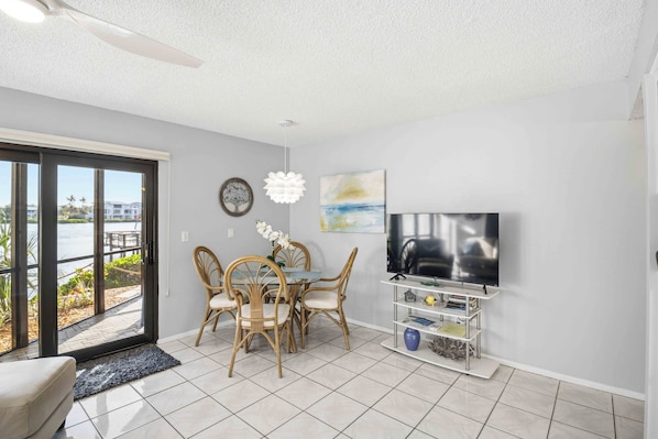 A dining area with a table and chairs, a television on a stand, and a view of a body of water through a glass door.