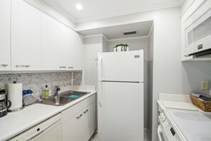 A compact kitchen with white cabinets, a built-in sink, a stainless steel refrigerator, and a microwave.