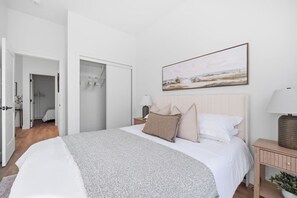Ein Schlafzimmer mit einem Bett, einem Nachttisch, einer Lampe, einem Gemälde und einem Kleiderschrank.