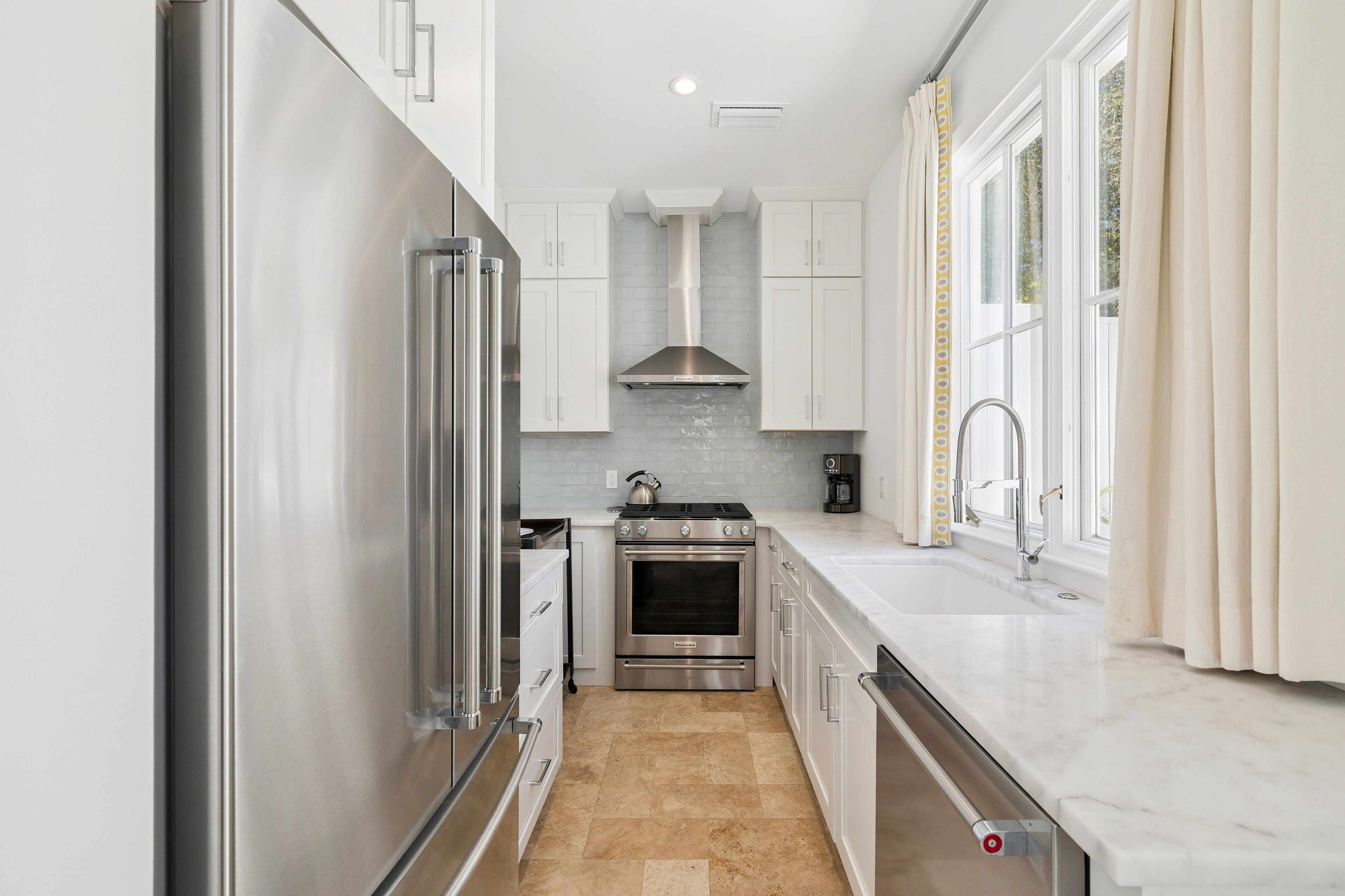A modern kitchen with stainless steel appliances, white cabinetry, and a tiled backsplash.
