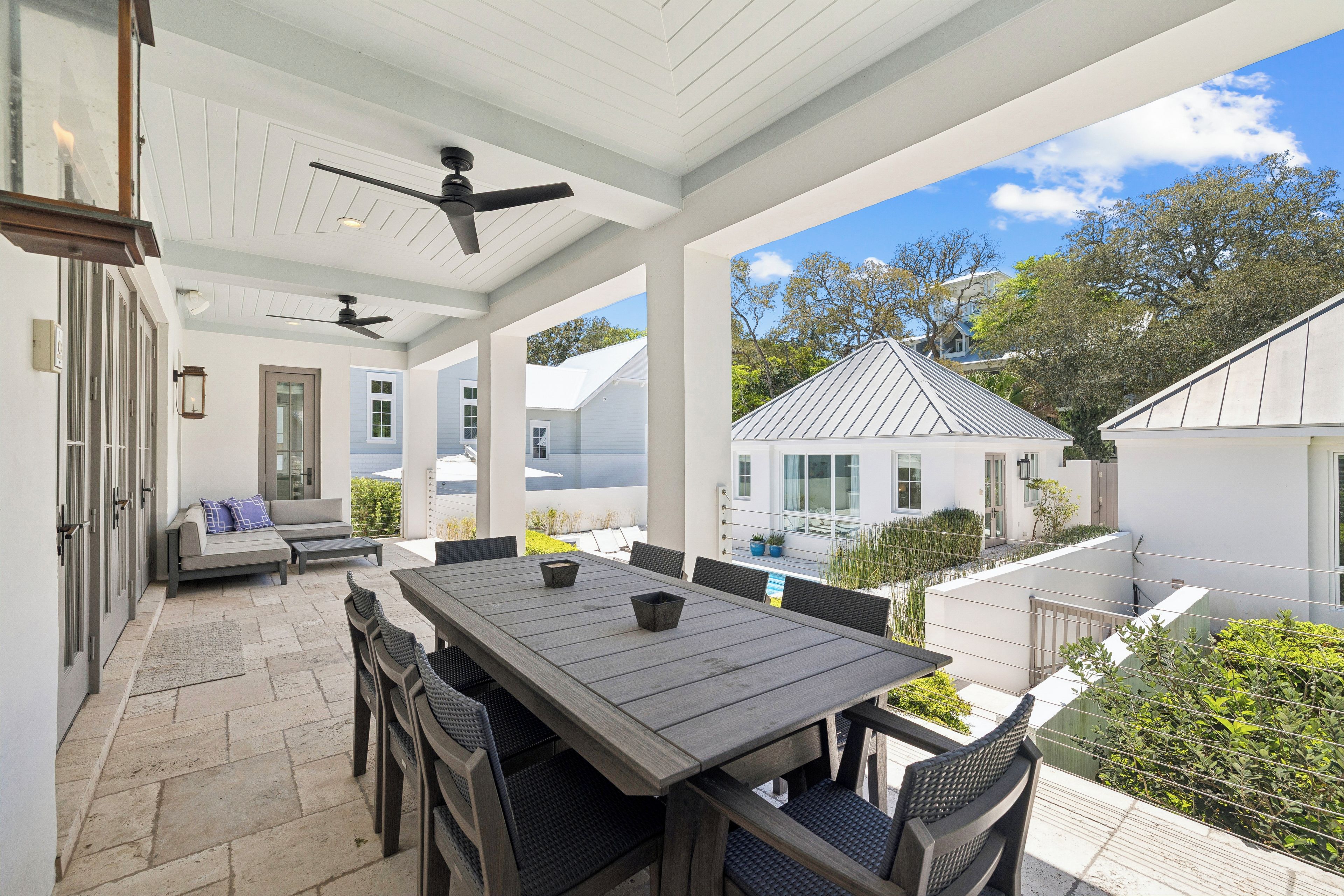 A covered patio area with a dining table and chairs, a ceiling fan, and a view of neighboring houses.