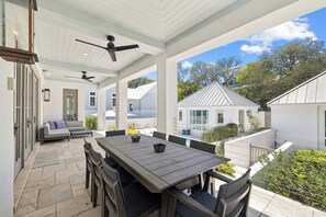 Un espacio de patio cubierto con mesa y sillas, ventilador de techo y vista a casas vecinas.