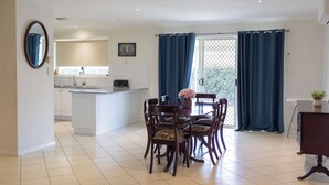 A dining area with a table and chairs, a kitchen with a sink and stove, and a view through a glass door. - The Apex, Pet-Friendly Dubbo Home (Dubbo)