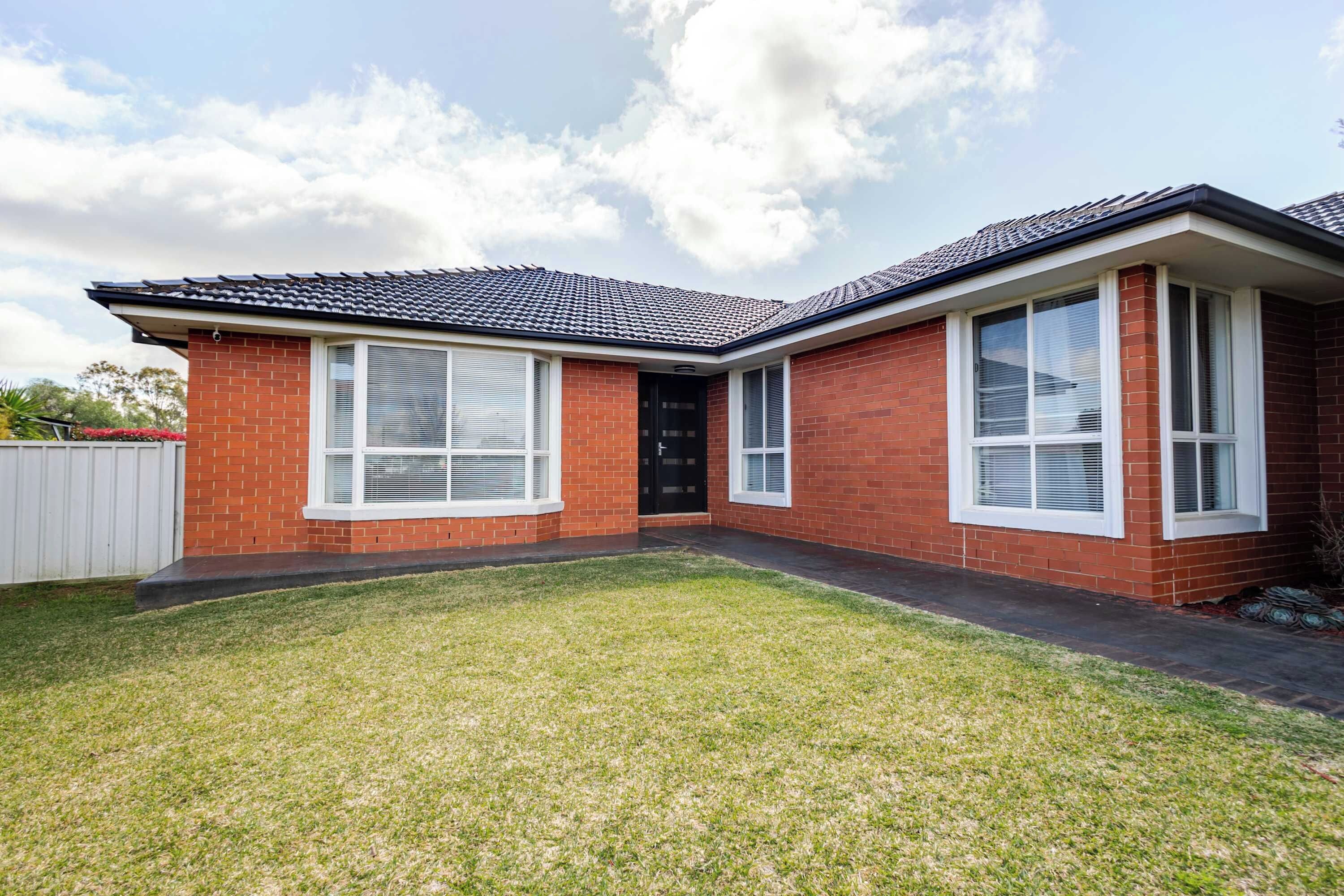 A two-story brick house with a tiled roof, large windows, and a well-maintained lawn.