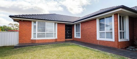 A two-story brick house with a tiled roof, large windows, and a well-maintained lawn.