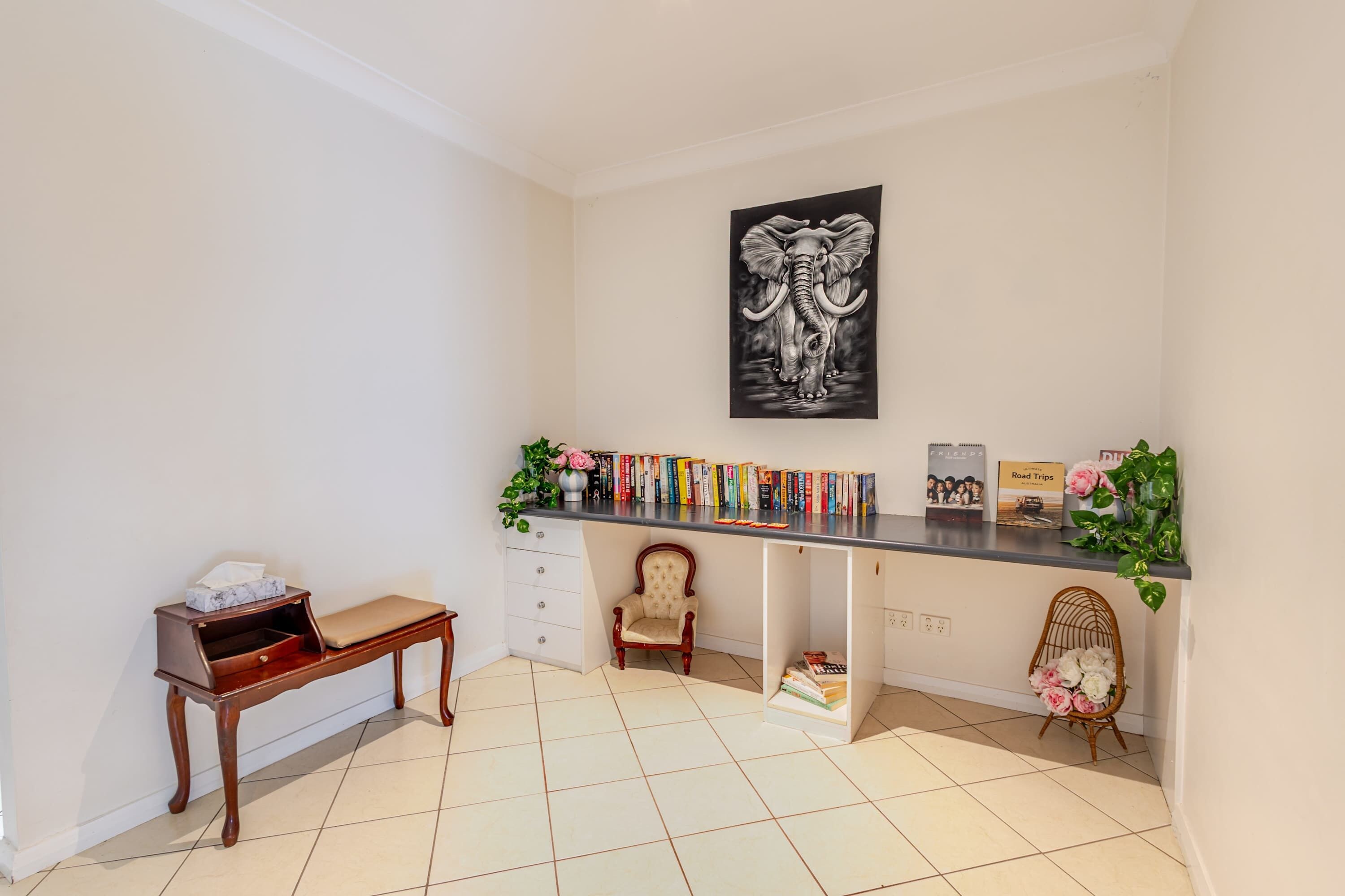 A room with a desk, a chair, a bench, a bookshelf, and a framed picture on the wall.