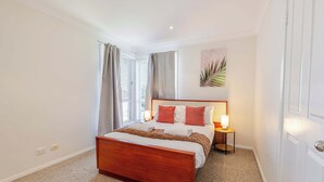 A hotel room with a wooden bed, a nightstand with a lamp, and a window with curtains. - The Apex, Pet-Friendly Dubbo Home (Dubbo)