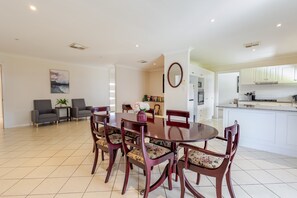 Un espace de repas moderne avec une grande table et des chaises en bois, une cuisine en arrière-plan et un tableau accroché au mur.