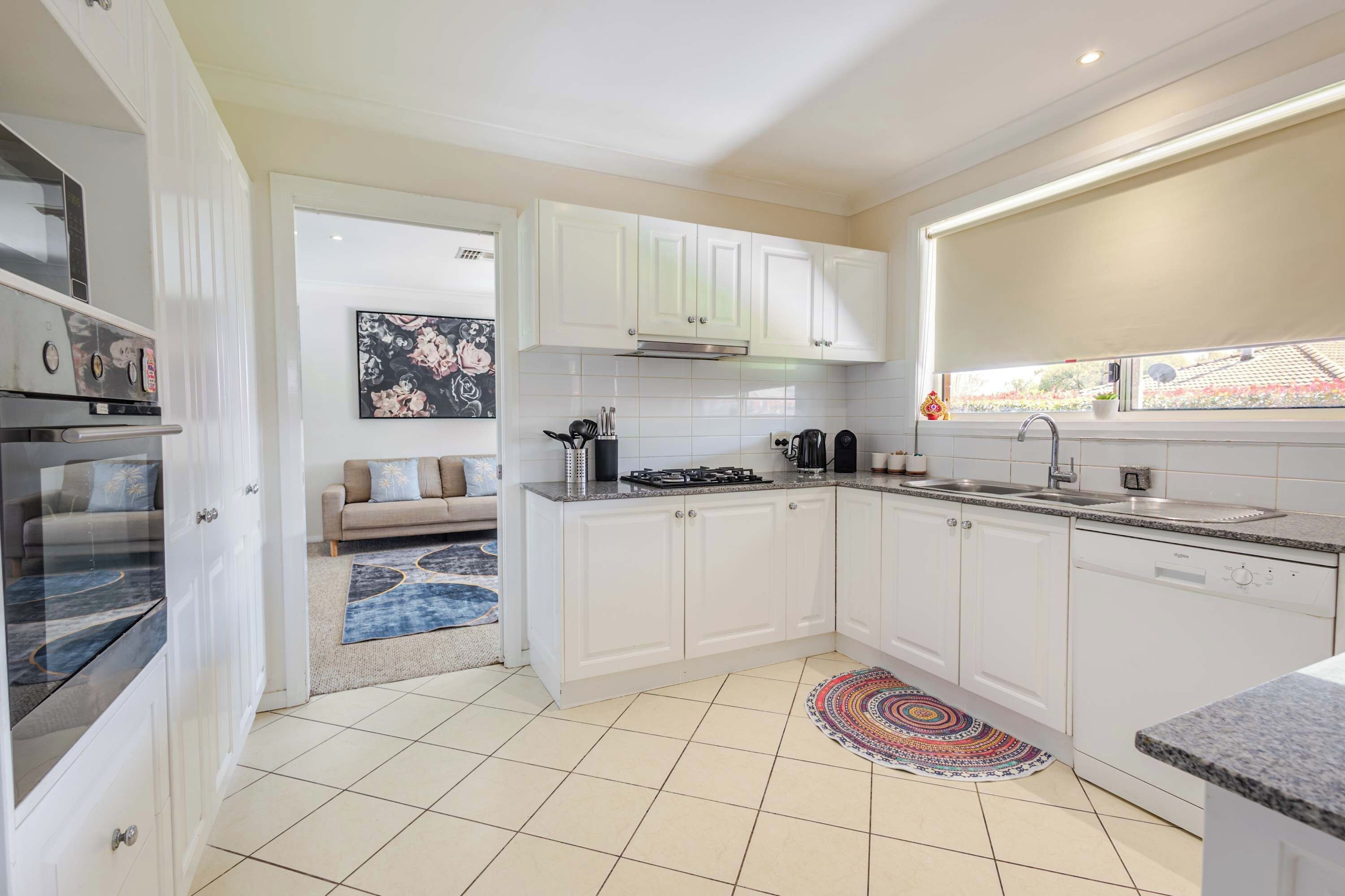 Une cuisine moderne avec des meubles blancs, une cuisinière à gaz, un four encastré et une fenêtre donnant sur l’extérieur.