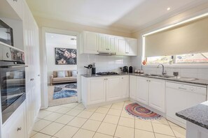 Une cuisine moderne avec des meubles blancs, une cuisinière à gaz, un four encastré et une fenêtre donnant sur l’extérieur.