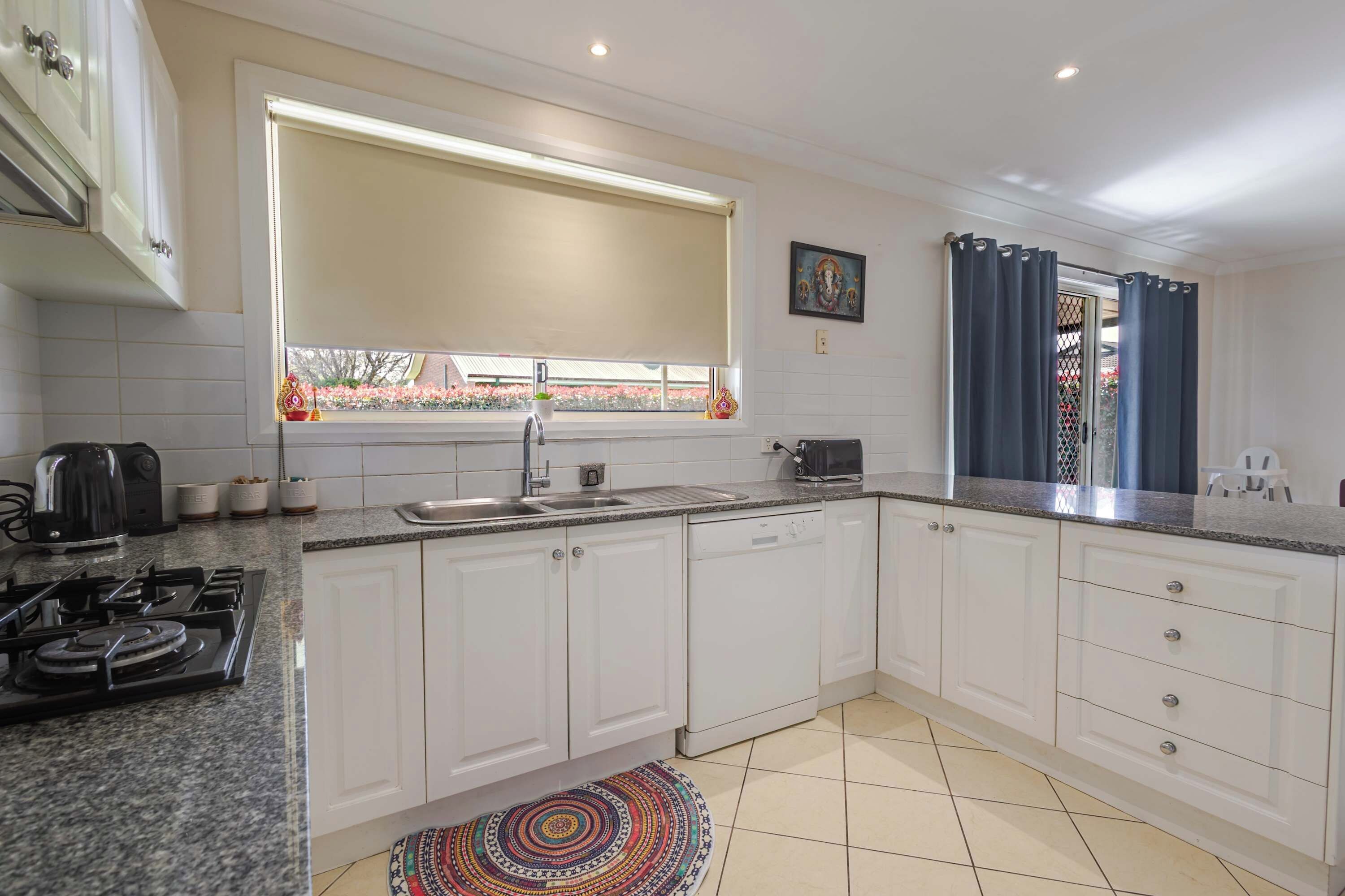 A modern kitchen with white cabinets, a gas stove, a sink, and a window with a view of a garden.