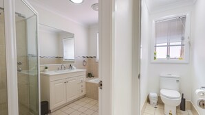 A modern bathroom with a glass shower enclosure, a white sink with a mirror above, and a toilet with a window above it. - The Apex, Pet-Friendly Dubbo Home (Dubbo)