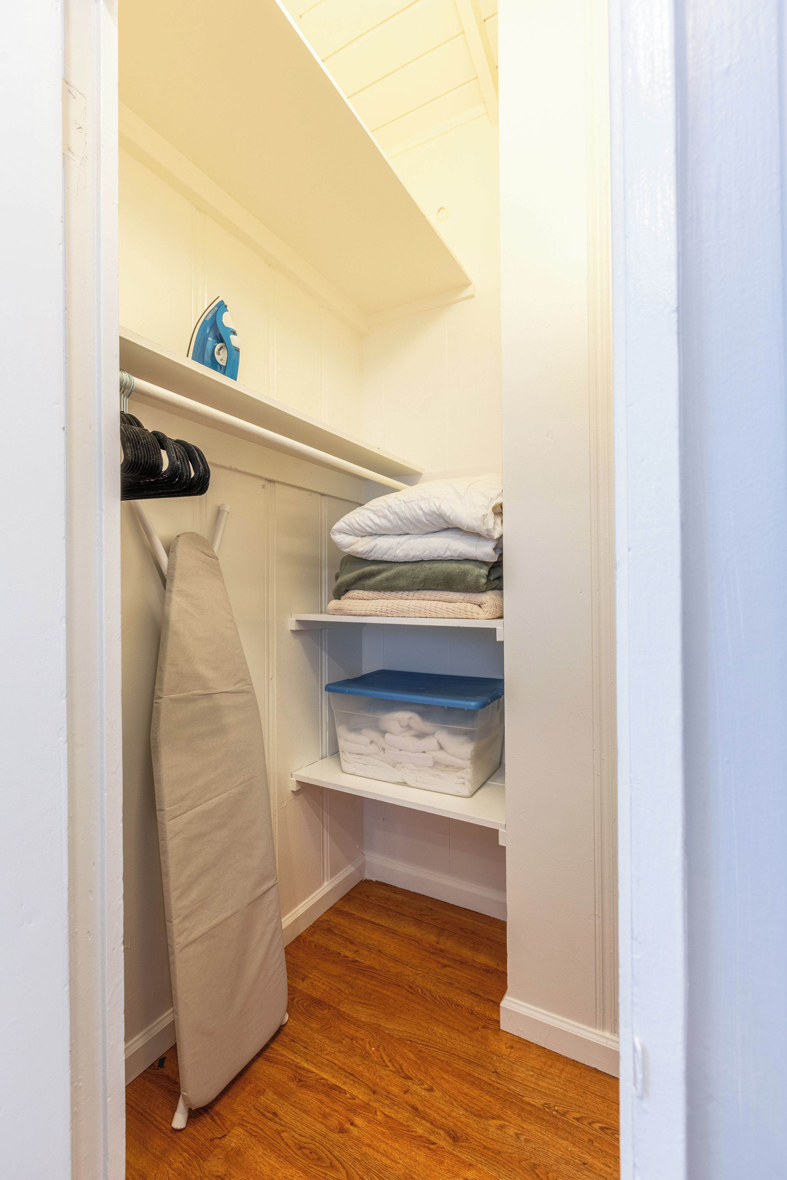 A walk-in closet with shelves for folded clothes, a hanging rack for shoes, and a storage bin.
