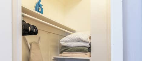 A walk-in closet with shelves for folded clothes, a hanging rack for shoes, and a storage bin.