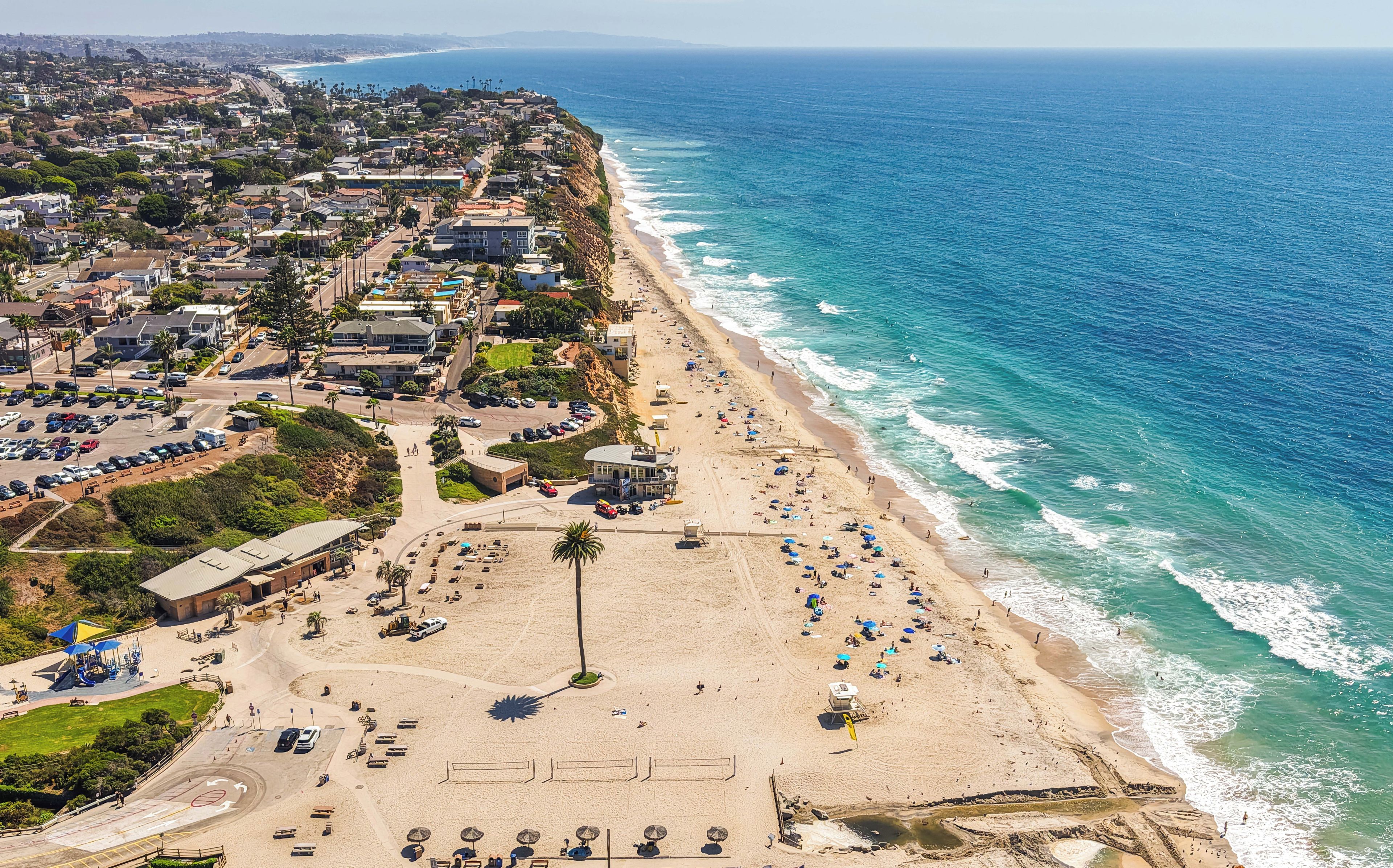 A coastal town with a beach, residential buildings, and a parking area.