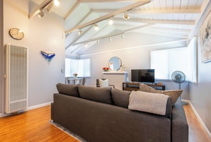 Ein modernes Wohnzimmer mit einer Couch, einem Fernseher und einem Essbereich im Hintergrund.