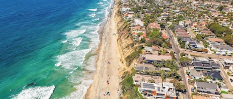 An aerial view of a coastal residential area with houses, a beach, and a clear view of the ocean.