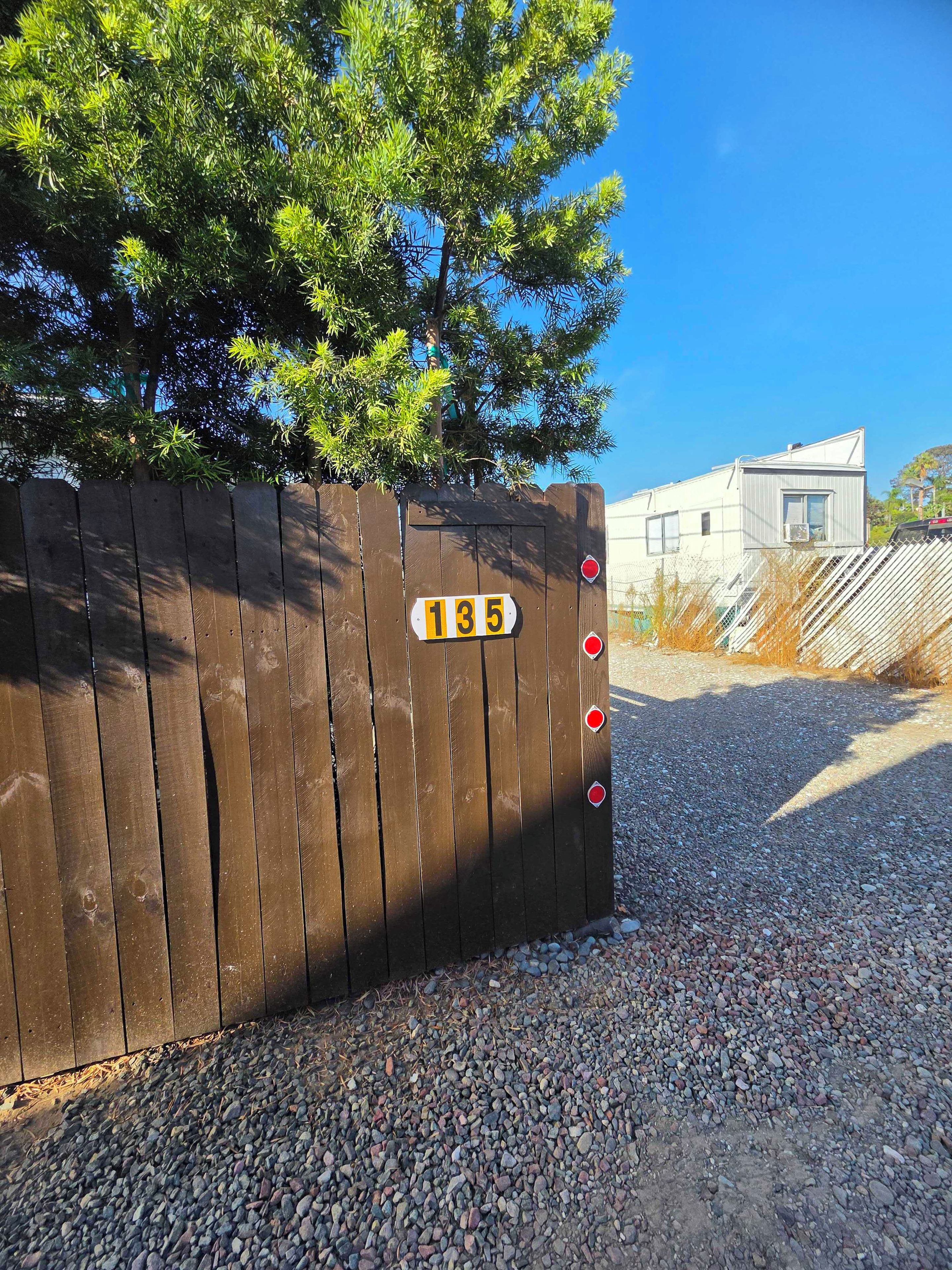 A wooden fence with a number sign, gravel ground, and a building in the background.