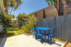 Un patio con mesa y sillas, una cerca de madera y un jardín con diversas plantas.