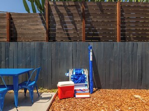 Eine Terrasse mit blauem Tisch und Stühlen, einem roten Kühlbox und einem blau-weißen Strandkorb vor einer Holzzaun.
