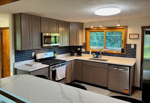 A modern kitchen with grey cabinets, a stainless steel stove, a microwave, and a window with a view of greenery. - Get the break you deserve, at the River Respite. (Memphis)