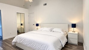 Une chambre à coucher avec un lit, des tables de chevet, un ventilateur de plafond et une porte.