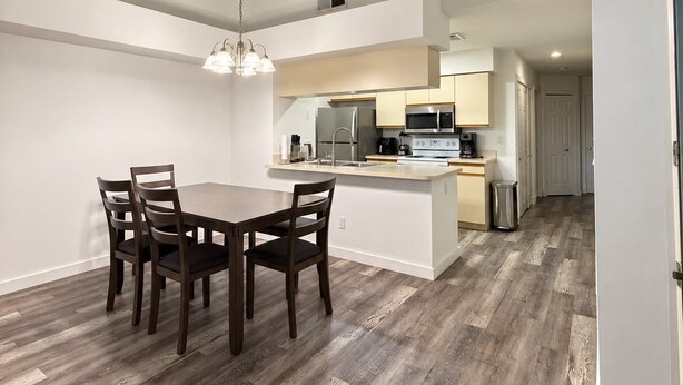 Une cuisine moderne avec un îlot central, un coin repas comprenant une table et des chaises, et un couloir menant à une autre pièce.