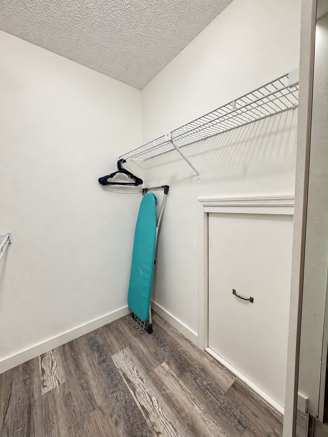 A corner room with a wooden floor, a white door, and a metal drying rack.