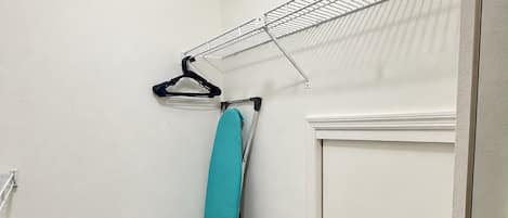 Une pièce d’angle avec un plancher en bois, une porte blanche et un étendoir à linge en métal.