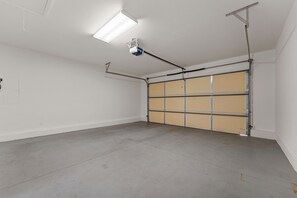 Garagem com piso de concreto, porta metálica e iluminação fluorescente no teto.