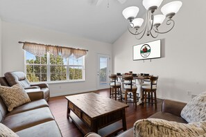 A living room with a sofa, a coffee table, a dining table with chairs, a chandelier, and a window with curtains. - Stay in the Heart of Branson • Gated 3BR Townhome • Pool • Near Shows, Shopping & Golf (Branson)